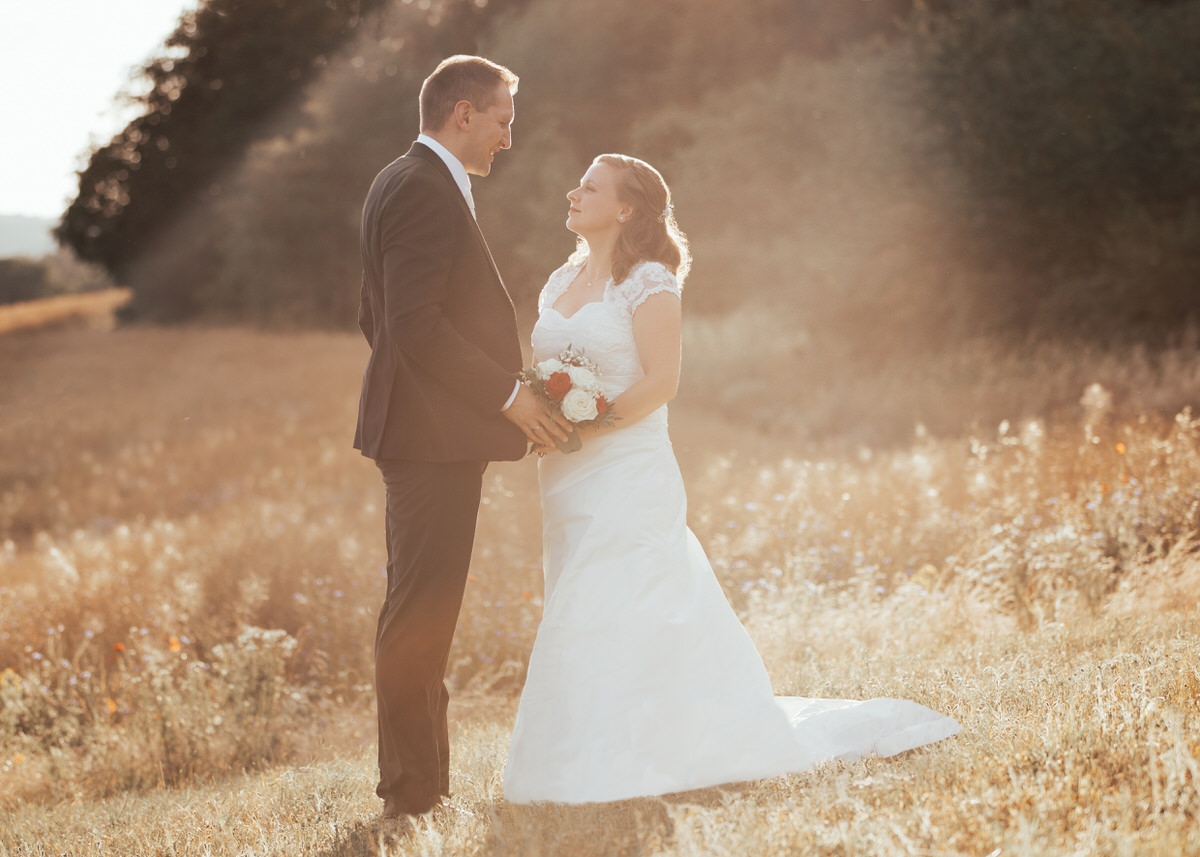 Brautpaar steh vor einem Kornfeld in der Sonne. Sie stehen sich gegenüber und schauen sich glücklich an. Fotografin: Claudia Nürnberger