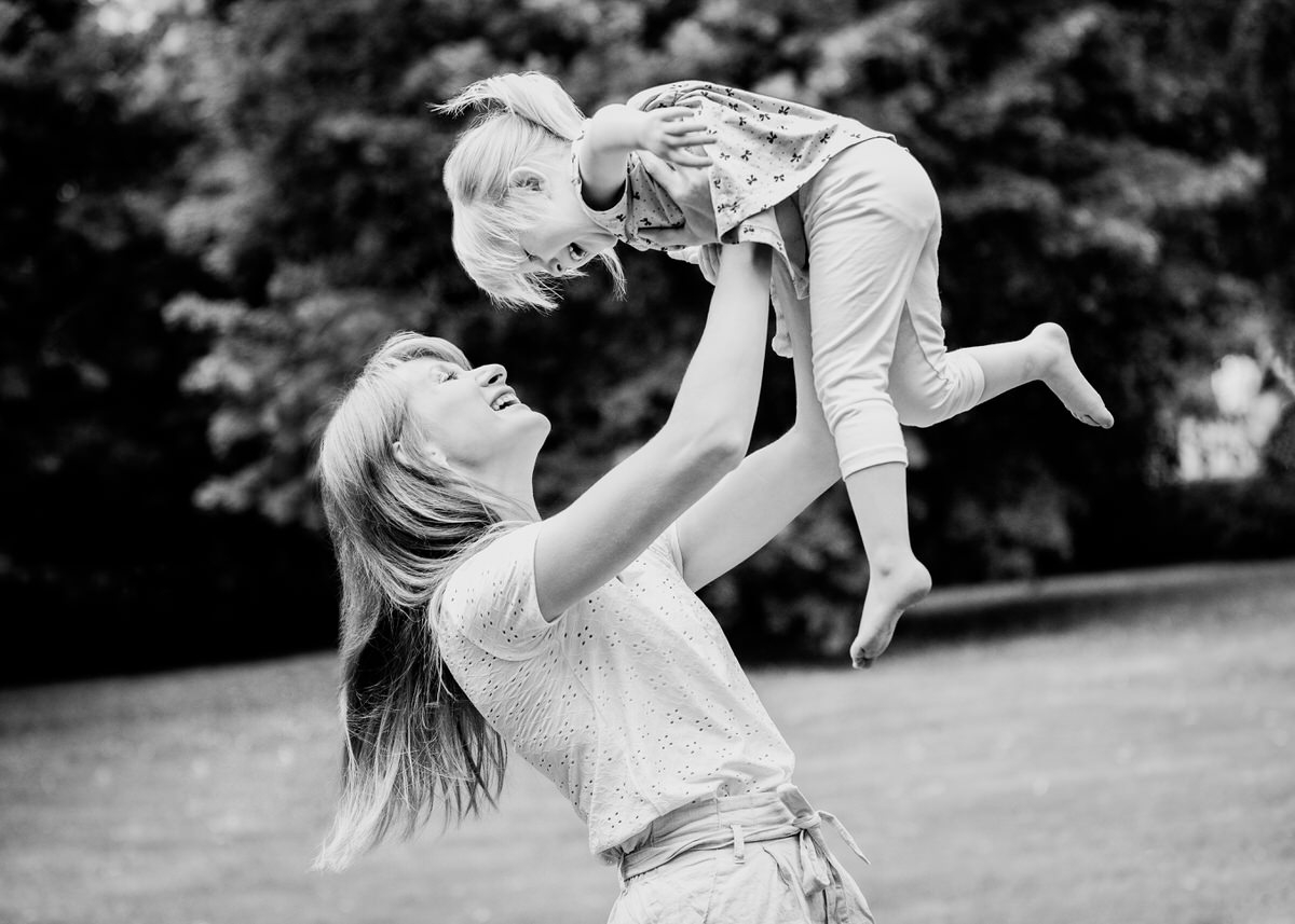Eine Mutter hebt ihre Tochter im Kindergartenalter über ihren Kopf und spielt mit ihr Flieger. Beide lachen sich ausgelassen an. Fotografin: Claudia Nürnberger
