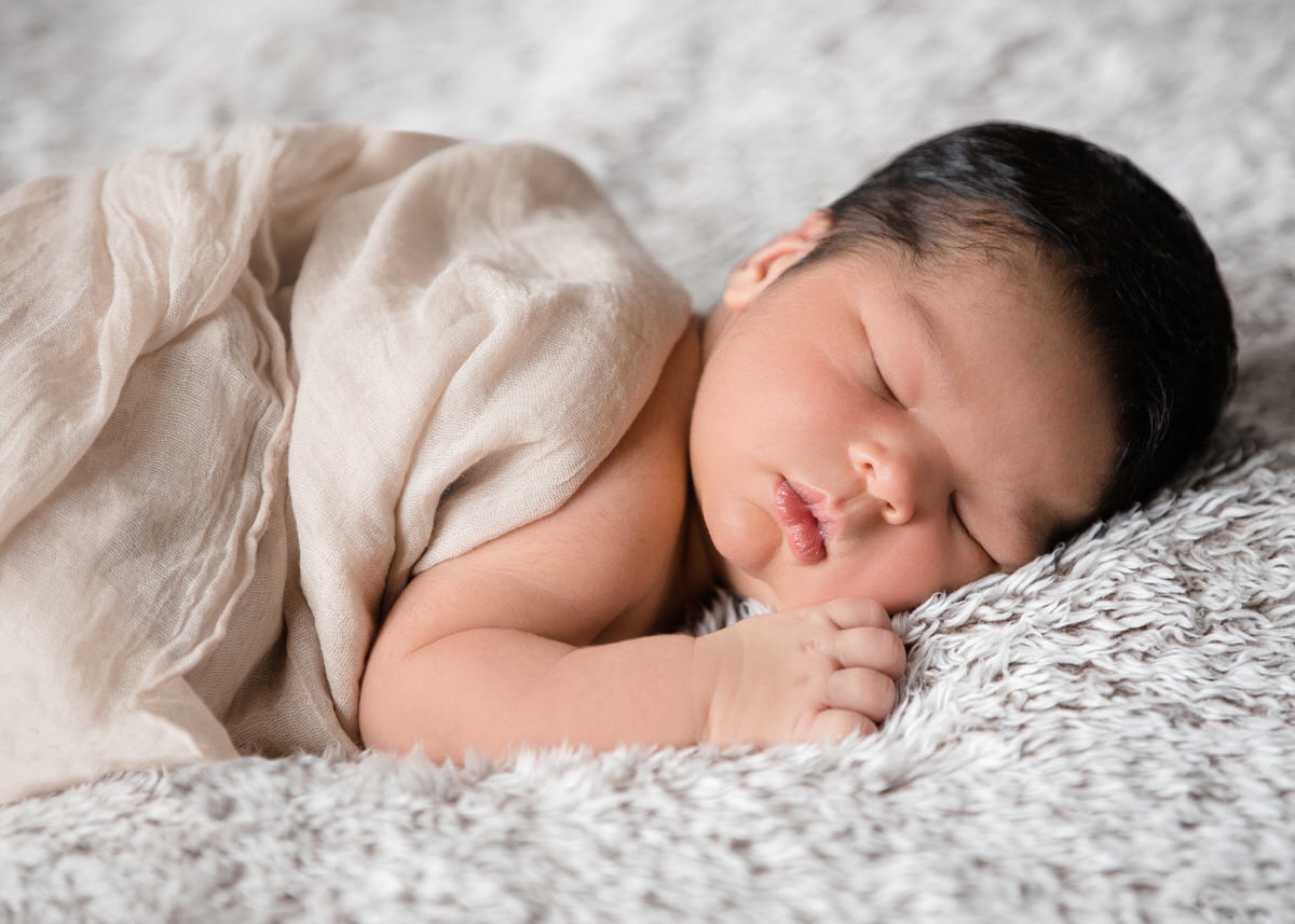 Neugeborenes Baby schläft auf einer kuschligen Decke zugedeckt mit einem Leinentuch. Fotografin: Claudia Nürnberger