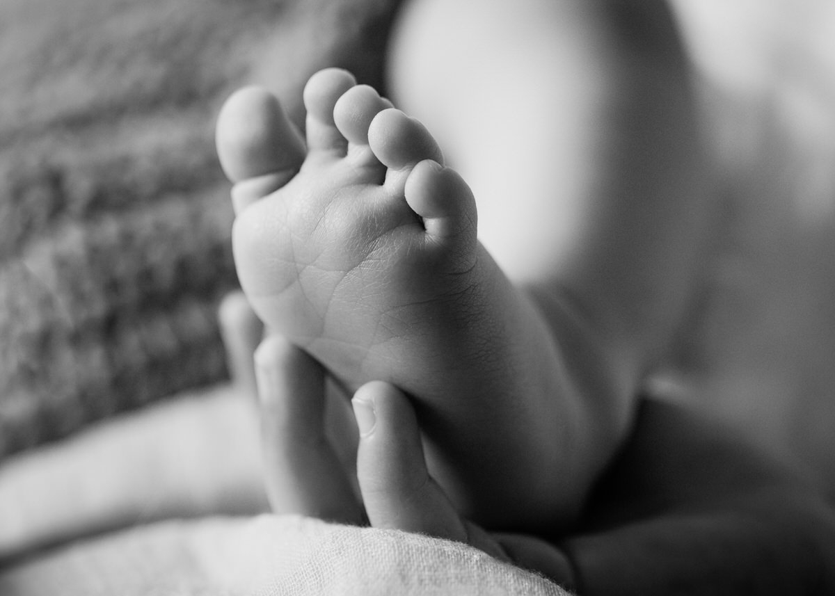 Fuß eines neugeborenen Babys liegt auf der Hand seiner großen Schwester. Fotografin: Claudia Nürnberger