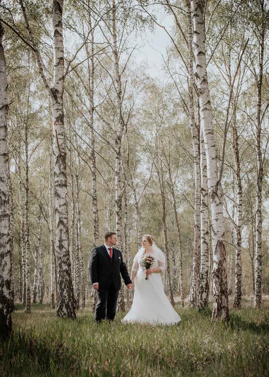 Brautpaar steht Händchen haltend in einem Birkenwald. Beide schauen sich verliebt an. Fotografin: Claudia Nürnberger / Berlin, Brandenburg